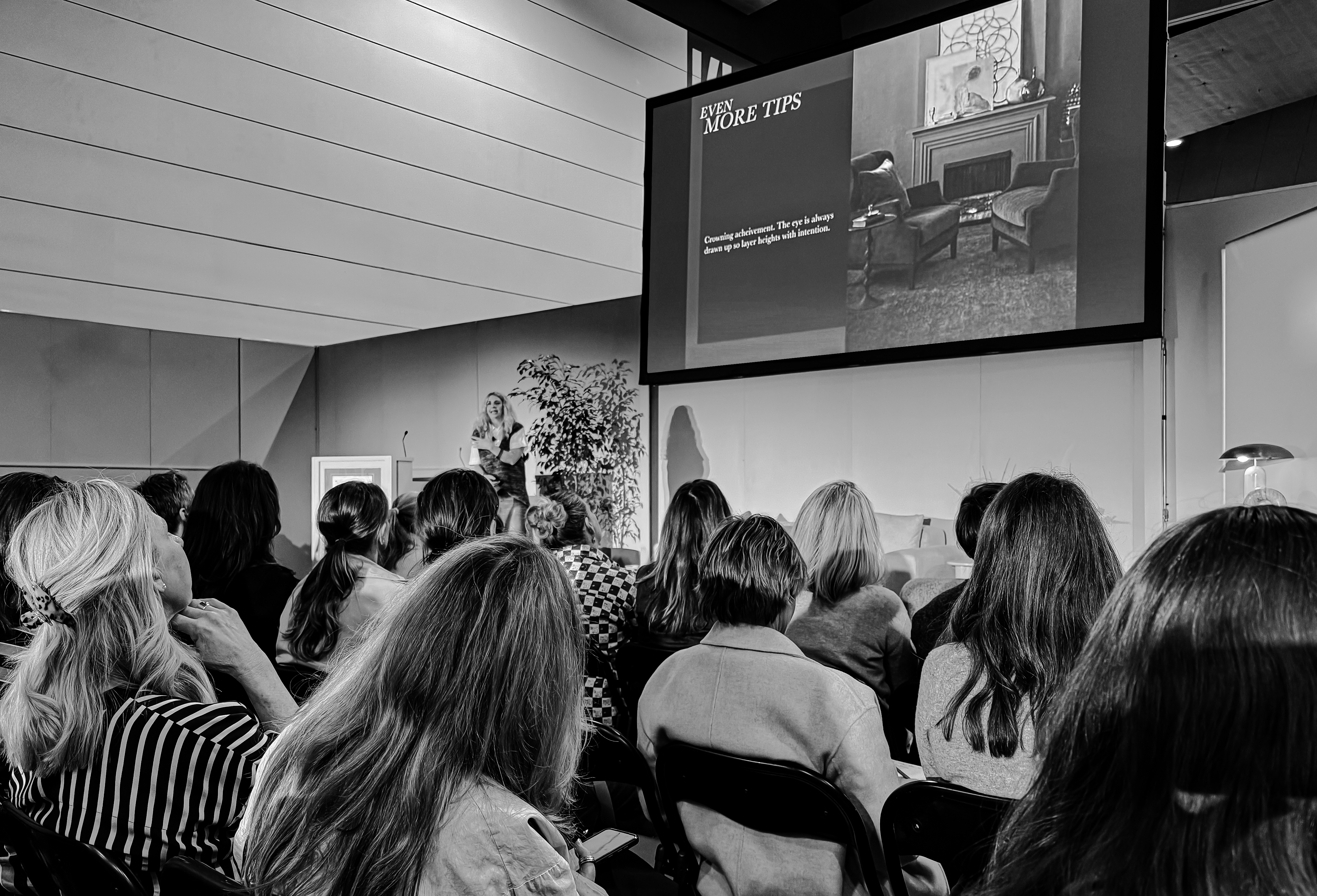 View from the audience as Lisa Elliott observes Abigail Ahern's presentation on Transforming Small Spaces with High-Impact Design at Decor & Design 2024. The stage is set with a large screen showcasing design visuals, while Abigail shares expert insights with the captivated crowd, offering innovative solutions for maximizing small interiors.