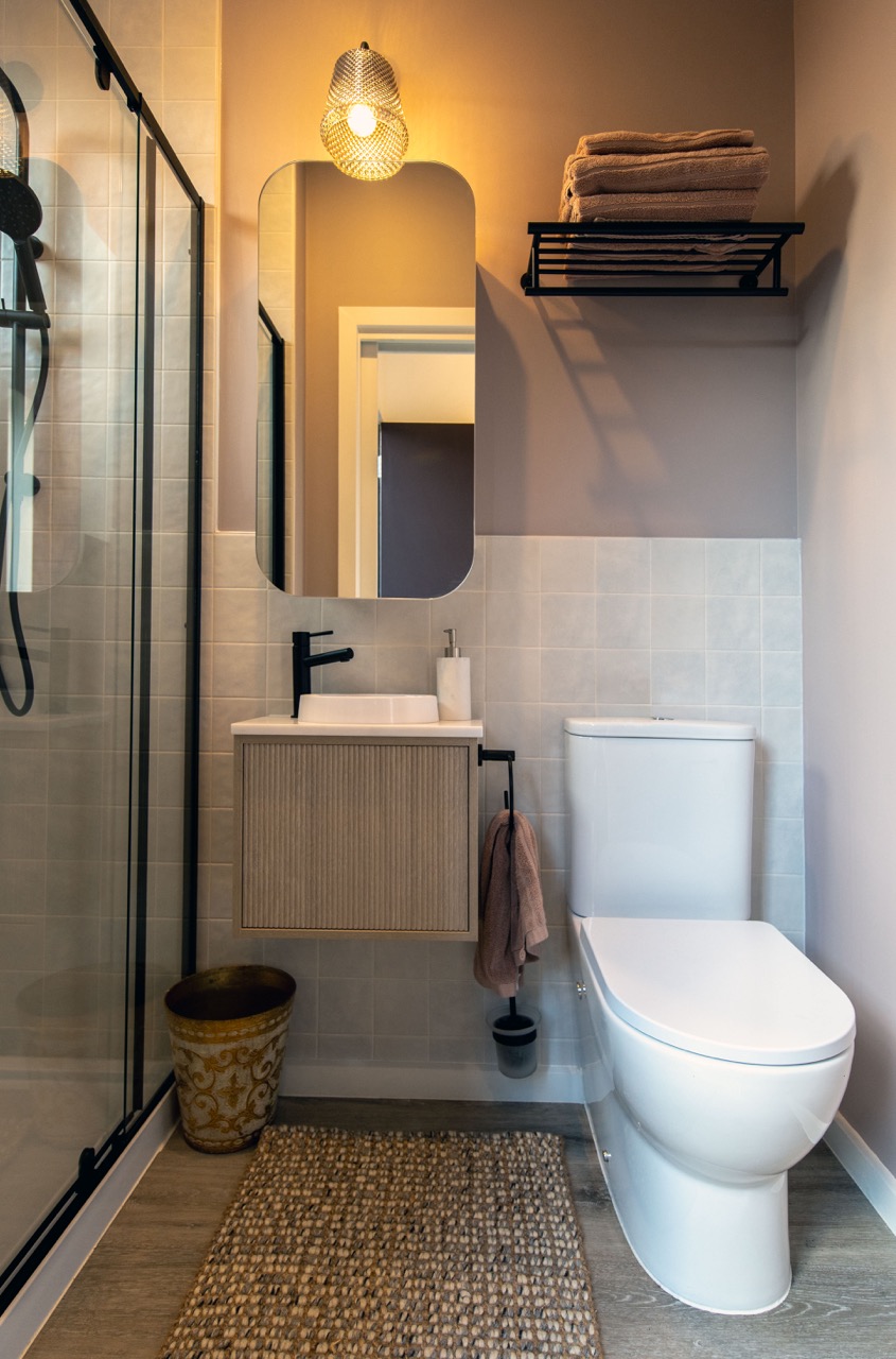 Compact luxury ensuite in studio space with full-size shower, heated towel rail, artisan tiles, and warm neutral tones designed by Lisa Elliott Interior Design