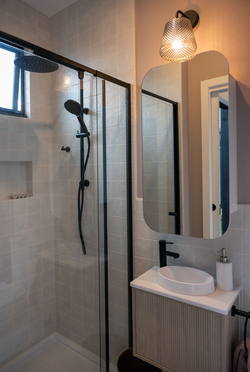 Compact luxury ensuite in Lisa Elliott's bespoke studio design, featuring neutral tones, a full-sized shower, heated towel rail, and modern black fixtures.